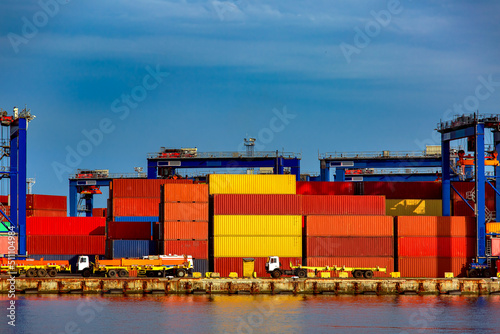 long truck in container depot in import and export area at port near sea on warehouse colorful marine containers with gantry container crane for loading freight to vehicle, day with blue sky, nobody.