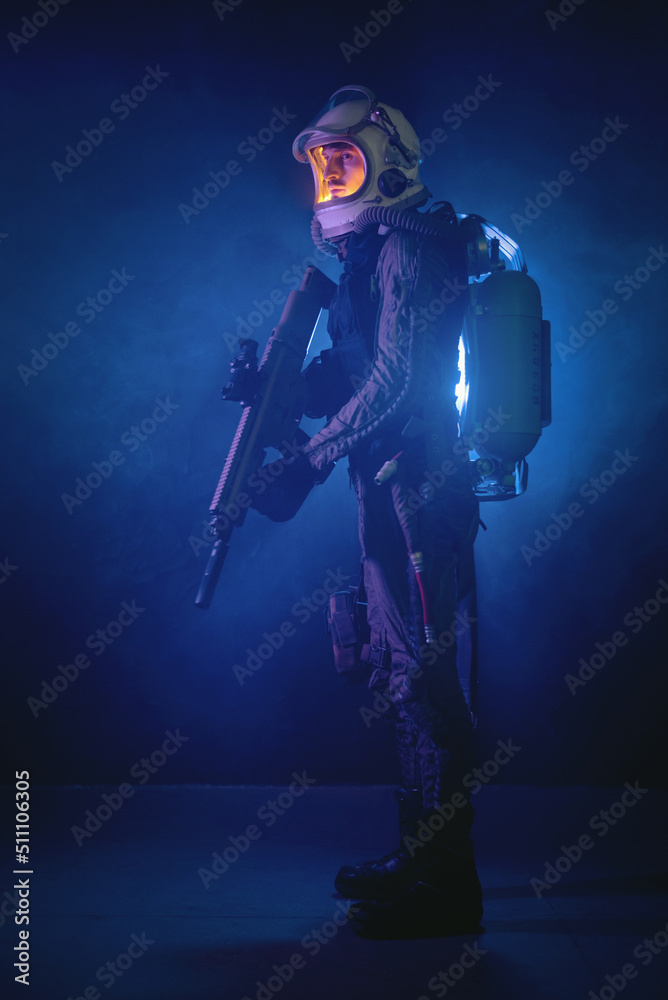 Spaceman or star trooper in the helmet and with rifle in the blue smoke. Science fiction concept.