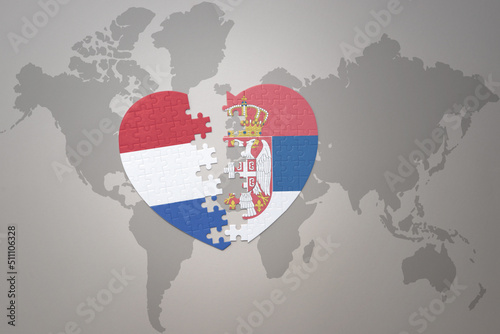 puzzle heart with the national flag of serbia and netherlands on a world map background.Concept.