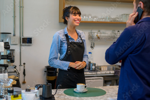 Young service minded barista woman with customer in coffee shop