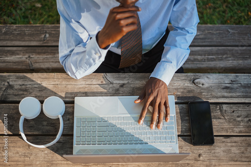 African male working with his computer at a wooden picnic area. He is focus.