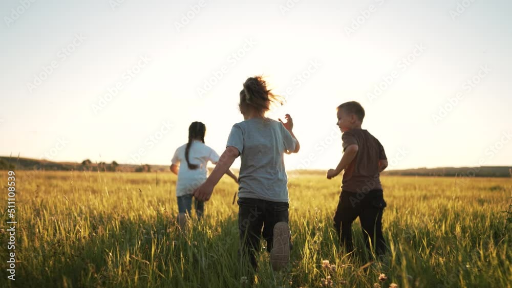 Group of happy children run walk on grass park. Cheerful smile of cute children in nature in meadow. Team of children are playing in green grass. Active movement and joy of children at sunset in field Group of happy children run walk on grass park. Cheerful smile of cute children in nature in meadow. Team of children are playing in green grass. Active movement and joy of children at sunset in field