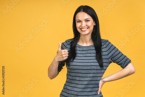 Portrait of happy smiling brunette girl in casual isolated over yellow background. Thumbs up.