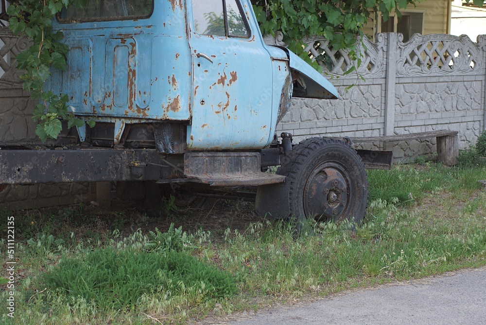one old disassembled truck with a blue cab stands on the street in green grass