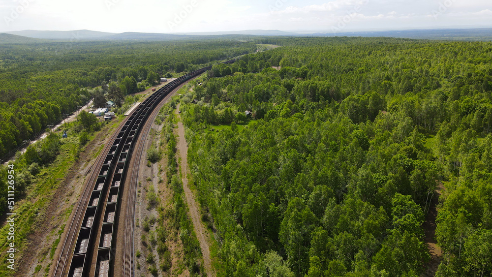Aerial View of the Long Trains in valley covered taiga, mountains near to dirt road with tracks in sunny summer day