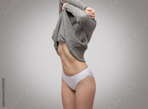 Фотография Slender woman takes off her gray knitted sweater