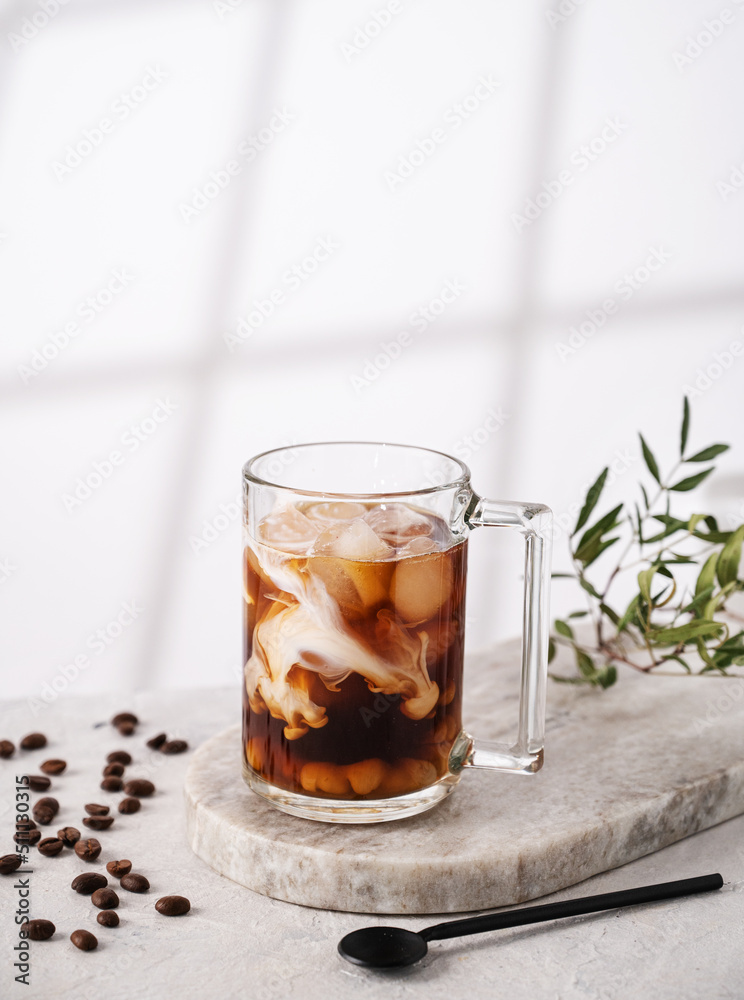 Iced coffee in a glass with cream, ice cubes and grains on a light marble background with morning shadows. The concept of a cold summer drink. Copy space Iced coffee in a glass with cream, ice cubes and grains on a light marble background with morning shadows. The concept of a cold summer drink. Copy space
