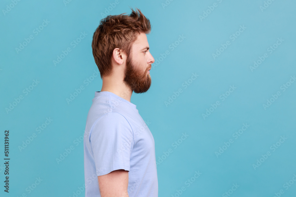 Side view portrait of confident strict bossy bearded man looking to side space with serious attentive face, unsmiling determined male. Indoor studio shot isolated on blue background. Side view portrait of confident strict bossy bearded man looking to side space with serious attentive face, unsmiling determined male. Indoor studio shot isolated on blue background.