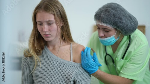 Young Caucasian beautiful woman feeling pain as nurse injecting coronavirus vaccine jab in shoulder. Portrait of charming patient in vaccination center getting shot on Covid-19 pandemic outbreak