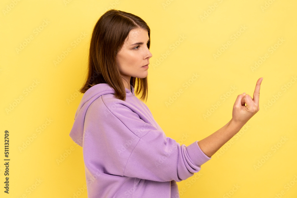 Side view portrait of rude vulgar woman showing middle fingers, impolite gesture of disrespect, looking with aggression hate, wearing purple hoodie. Indoor studio shot isolated on yellow background. Side view portrait of rude vulgar woman showing middle fingers, impolite gesture of disrespect, looking with aggression hate, wearing purple hoodie. Indoor studio shot isolated on yellow background.