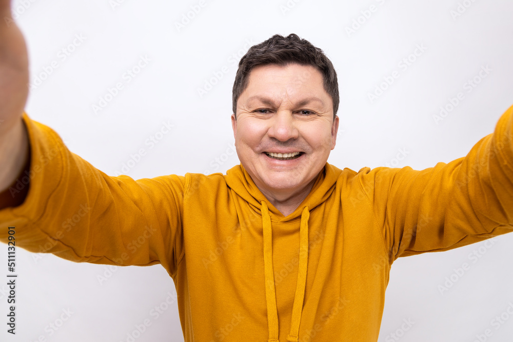 Portrait of smiling middle aged man taking selfie, looking at camera with happy expression and toothy smile POV, wearing urban style hoodie. Indoor studio shot isolated on white background. Portrait of smiling middle aged man taking selfie, looking at camera with happy expression and toothy smile POV, wearing urban style hoodie. Indoor studio shot isolated on white background.