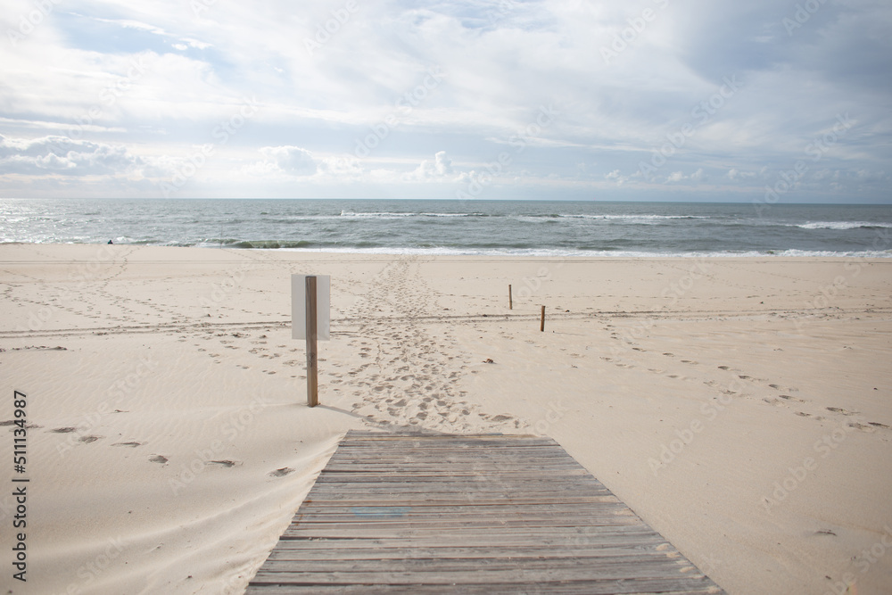 Beautiful ocean with a wooden walkway and sign on the sandy beach. Amazing view of the sea with clouds