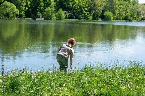 A woman on the riverbank fishing with a fishing rod. Fishing in the summer early in the morning. Saint Petersburg, Tsarskoye Selo.06.06.2022