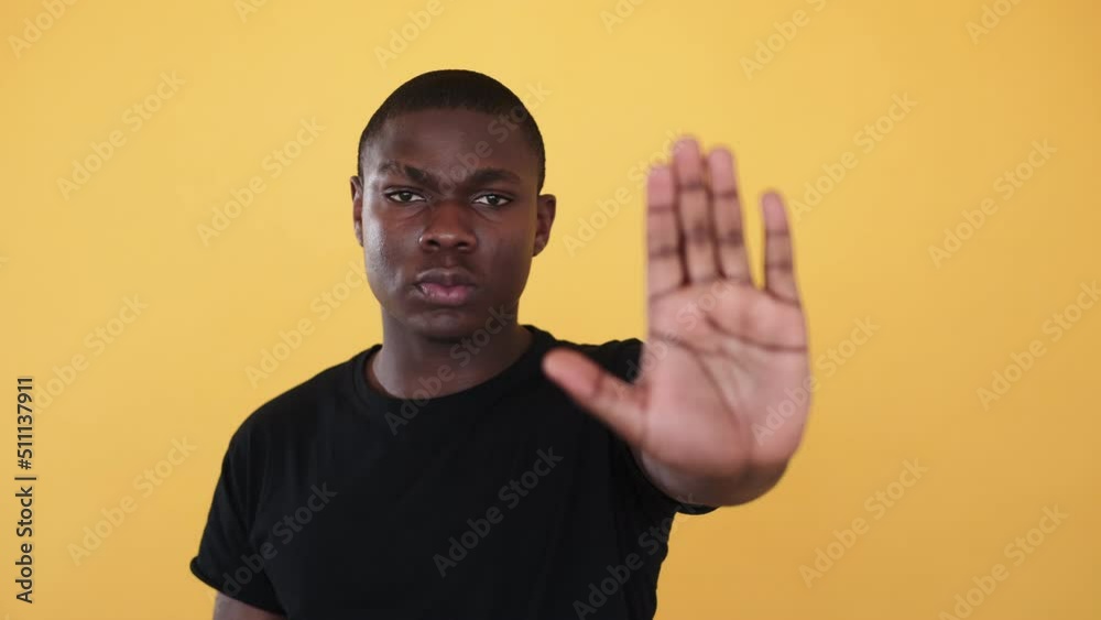 Stop racism. Black man showing blocking gesture. Racial discrimination blockage. Serious rejecting man showing refusal hand sign isolated on orange background. Stop racism. Black man showing blocking gesture. Racial discrimination blockage. Serious rejecting man showing refusal hand sign isolated on orange background.