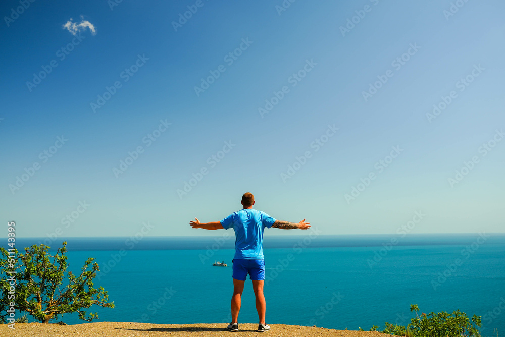 a man standing on a hill raised his hands up enjoying the view of the sea and blue sky