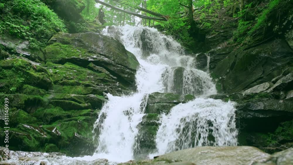 Waterfall. Water flows over stones overgrown with moss in a green forest.
