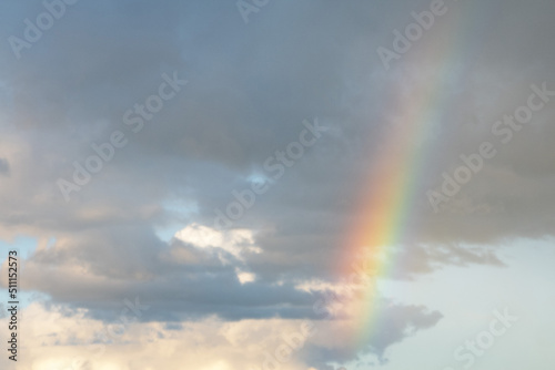 A multi-colored rainbow spread across a cloudy blue sky.