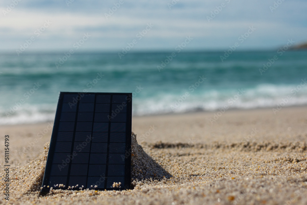 A black solar panel with squares stands on the sand against the background of the ocean. Allernative energy sources. Ecology. Environmentally friendly energy cleaners. Renewable energy. Idea. Concept A black solar panel with squares stands on the sand against the background of the ocean. Allernative energy sources. Ecology. Environmentally friendly energy cleaners. Renewable energy. Idea. Concept