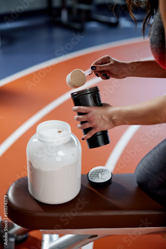 A fit sportswoman is mixing protein powder and making a protein drink in a gym.