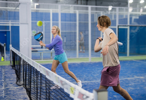 Portrait of a focused fifteen-year-old boy-athlete and a European woman tennis player playing padel on the court