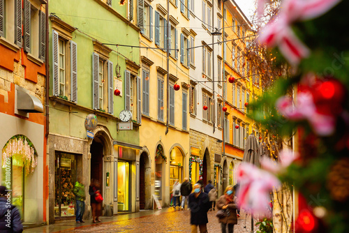 View of typical narrow cobbled street of historical Italian city of Bergamo with colorful buildings and traditional Christmas decorations during winter holidays