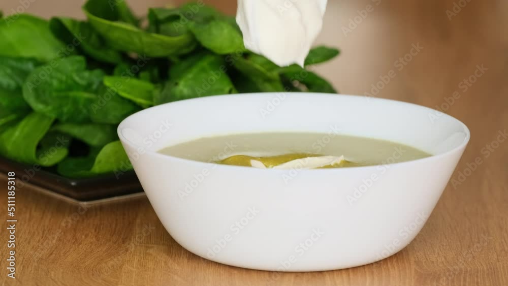Bowl of healthy green spinach soup with cream. Chef garnishing Spinach or broccoli soup with cream. Spinach creamy soup. Adding sour cream into soup closeup Bowl of healthy green spinach soup with cream. Chef garnishing Spinach or broccoli soup with cream. Spinach creamy soup. Adding sour cream into soup closeup