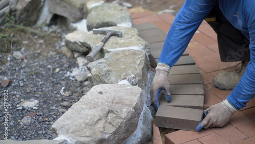 Closeup of putting brick pavers in place along an edge of a rock wall.