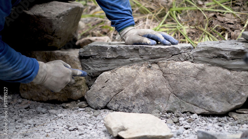 Closeup of putting mortar between large stones in a rock wall design in hardscaping landscaping project.