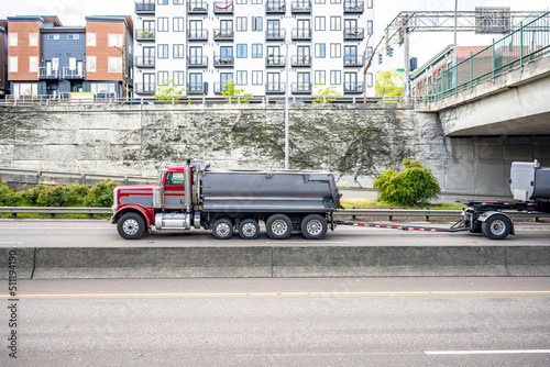 Loaded big rig tip truck with additional axles for heavy load and with two tipper trailers driving on the city highway road intersection