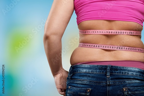 Unrecognizable fat plump plus-size overweight woman standing, showing excess naked belly, measuring waist with tape. Dieting, unhealthy food, obesity. © BillionPhotos.com