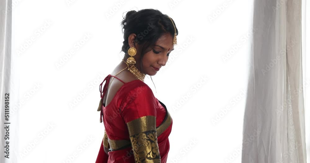 Indian woman wearing red orange traditional royal saree and jewellery showing turning smile bright window backlight Indian woman wearing red orange traditional royal saree and jewellery showing turning smile bright window backlight