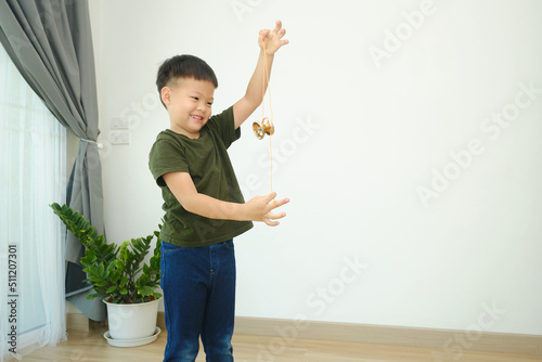 Cute little Asian school boy child having fun learning how to play with a yo-yo toy alone in living room at home, Photo in real life interior