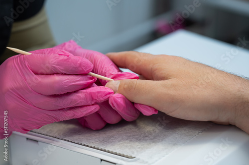 Manicurist removes cuticles with an orange stick to a male client. 