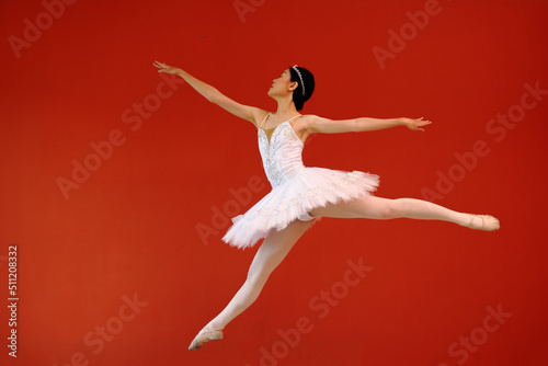 Beautiful Asian woman ballet dancer practice dance jump move wearing tutu at home red orange background wall