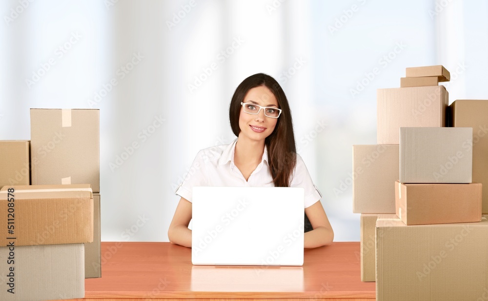 Portrait of businesswoman sitting at table, packing boxes with orders, working on laptop Portrait of businesswoman sitting at table, packing boxes with orders, working on laptop