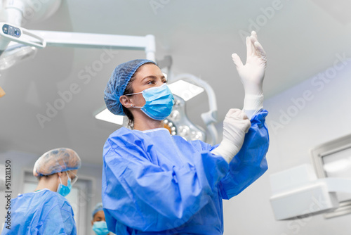 Portrait of beautiful female doctor surgeon putting on medical gloves standing in operation room. Surgeon at modern operating room