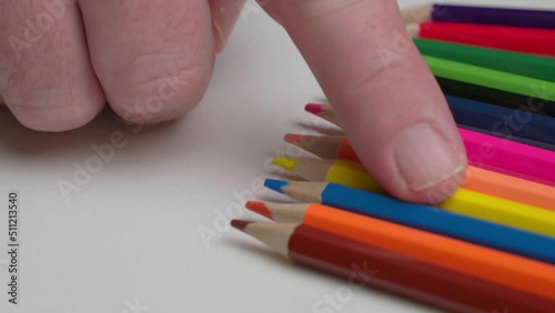 Male finger pulls out a yellow pencil from a set of colored pencils, close-up. The artist chooses a colored pencil from a set on a white table