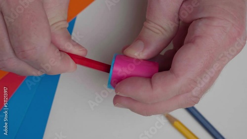 The artist sharpens a red pencil, top view. Close-up of a man's hand with a sharpener and a drawing pencil