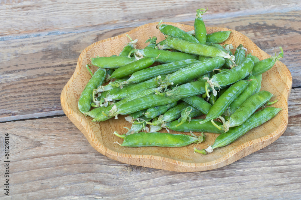 Closeup shot of fresh green peas with seed pods in the plate with wooden background Closeup shot of fresh green peas with seed pods in the plate with wooden background