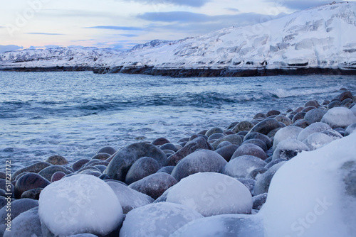 Winter seascape, beautiful sky and cold Barents Sea. Snow-covered rocky shore with large pebbles. Sea and blue sky. In the Far North. Russia photo