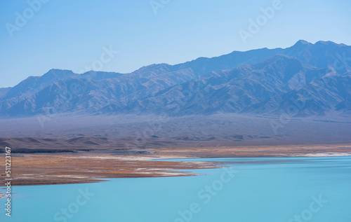 A turquoise lake in the middle of a lifeless valley with mountains in a blue haze in the distance. Gray, dull mountains with a bright lake.