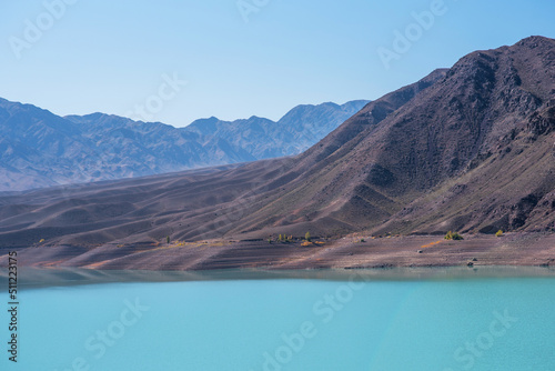 A turquoise lake in the middle of a lifeless valley with mountains in a blue haze in the distance. Gray, dull mountains with a bright lake.
