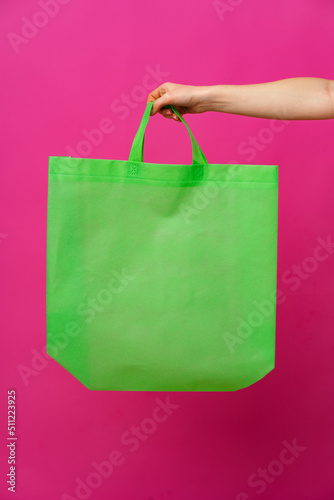 Female hand holding eco or reusable shopping bag against pink background