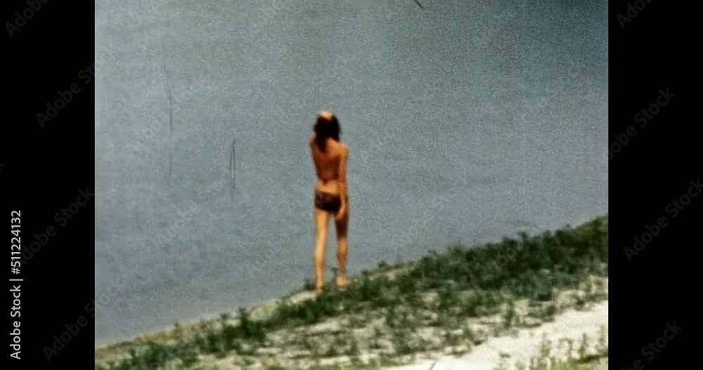 Woman in bikini walks on river beach at sunny summer. Beautiful model happy girl in swimsuit resting near lake water. Holiday vacation. Vintage color film. Retro 80s, 90s archive. 1980s-1990s. 4k
