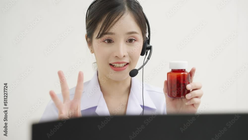 Close up of a Asian female doctor wearing a lab coat sitting in the medical room at hospital looking at a computer screen and making a video call with headphone recommend medication to the patient Close up of a Asian female doctor wearing a lab coat sitting in the medical room at hospital looking at a computer screen and making a video call with headphone recommend medication to the patient