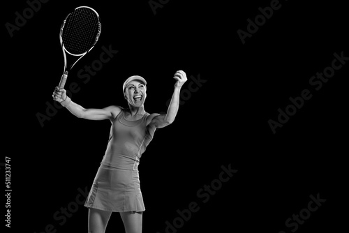 Monochrome portrait of amazed smiling woman holding racket and playing tennis on black background © Denys Kurbatov