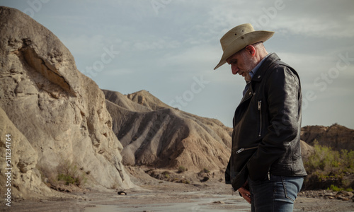 Adult man in cowboy hat in desert against rock and sky