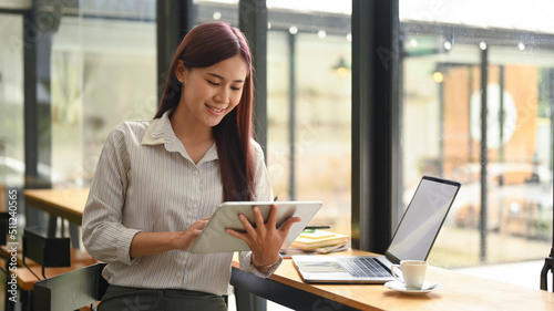 Smiling female manager sitting at wooden counter in modern office and using digital tablet