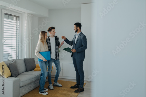 Happy young couple buying their new home and receiving keys from real estate agent