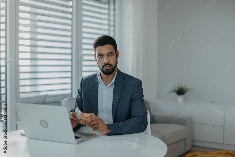 Depressed businessman man counting euro money working on computer at office desk and looking at camera, inflation concept.